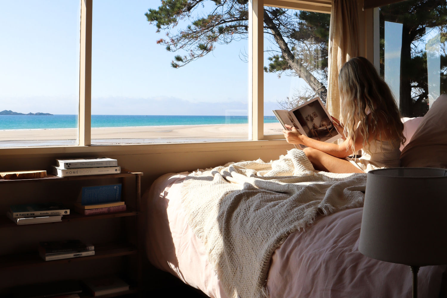 Woman reading book in bedroom with beach view